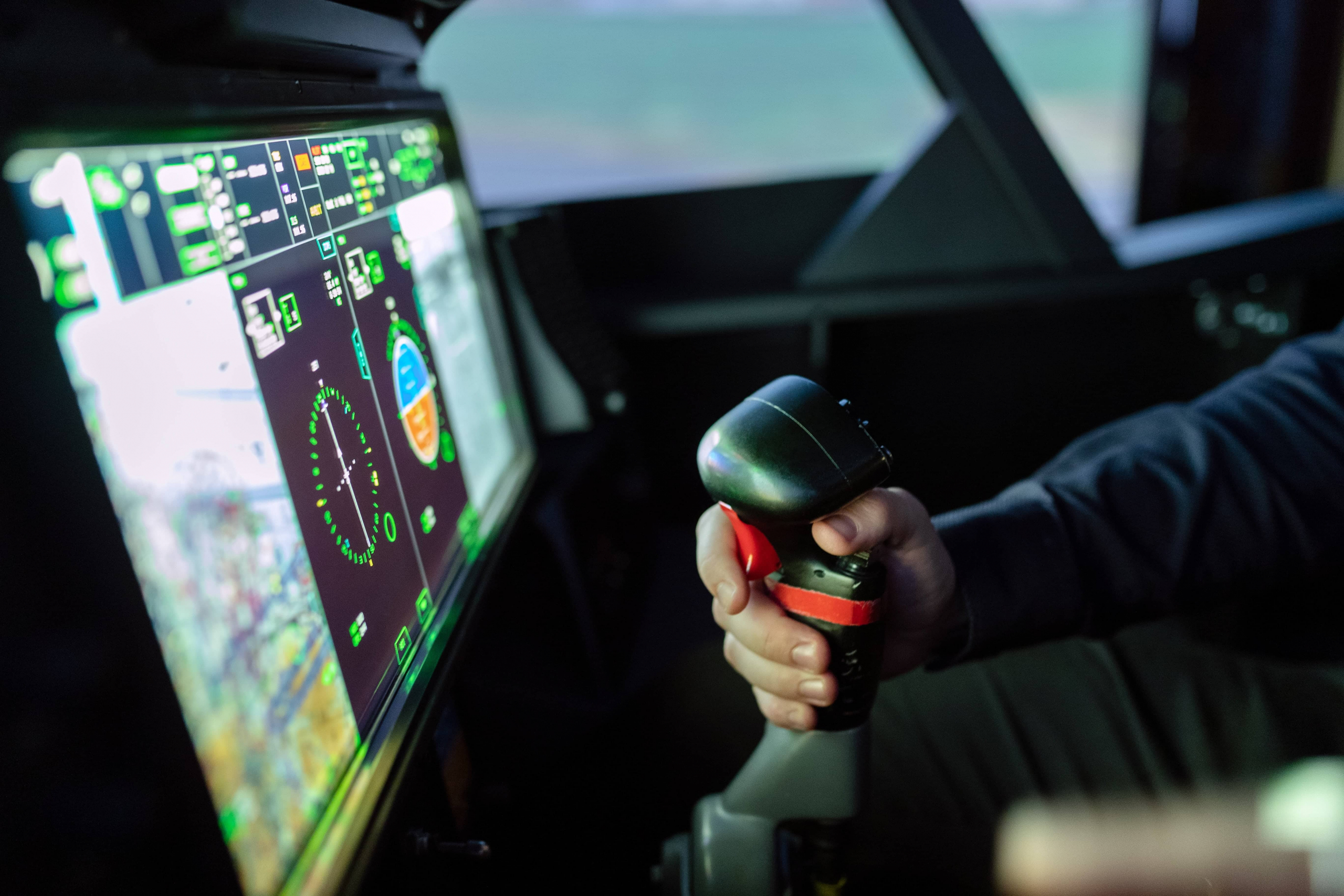 Photo d'une main qui tiens un joystick et un écran où on y voit un jeu de vidéo d'avion