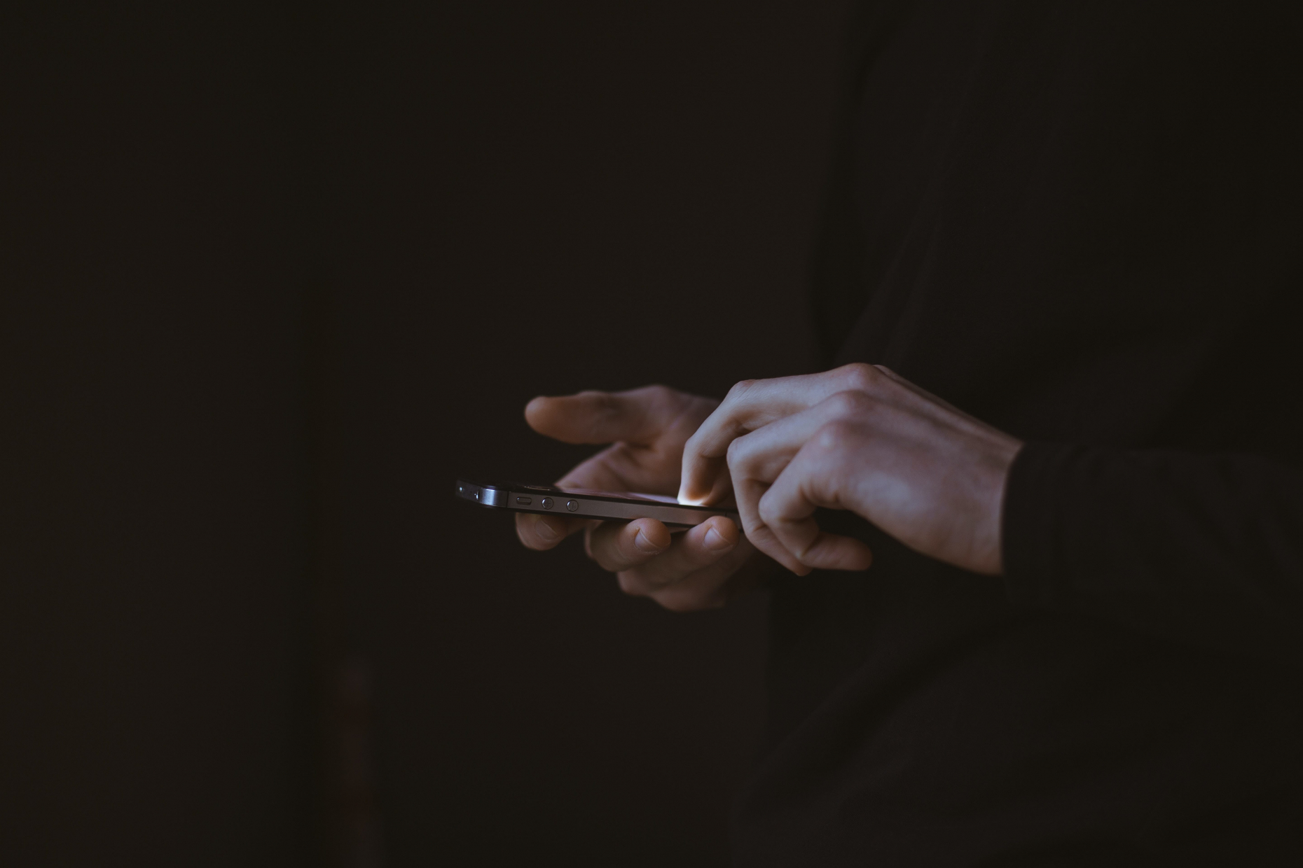 Photo de main d'un homme tenant un téléphone sur un fond sombre,